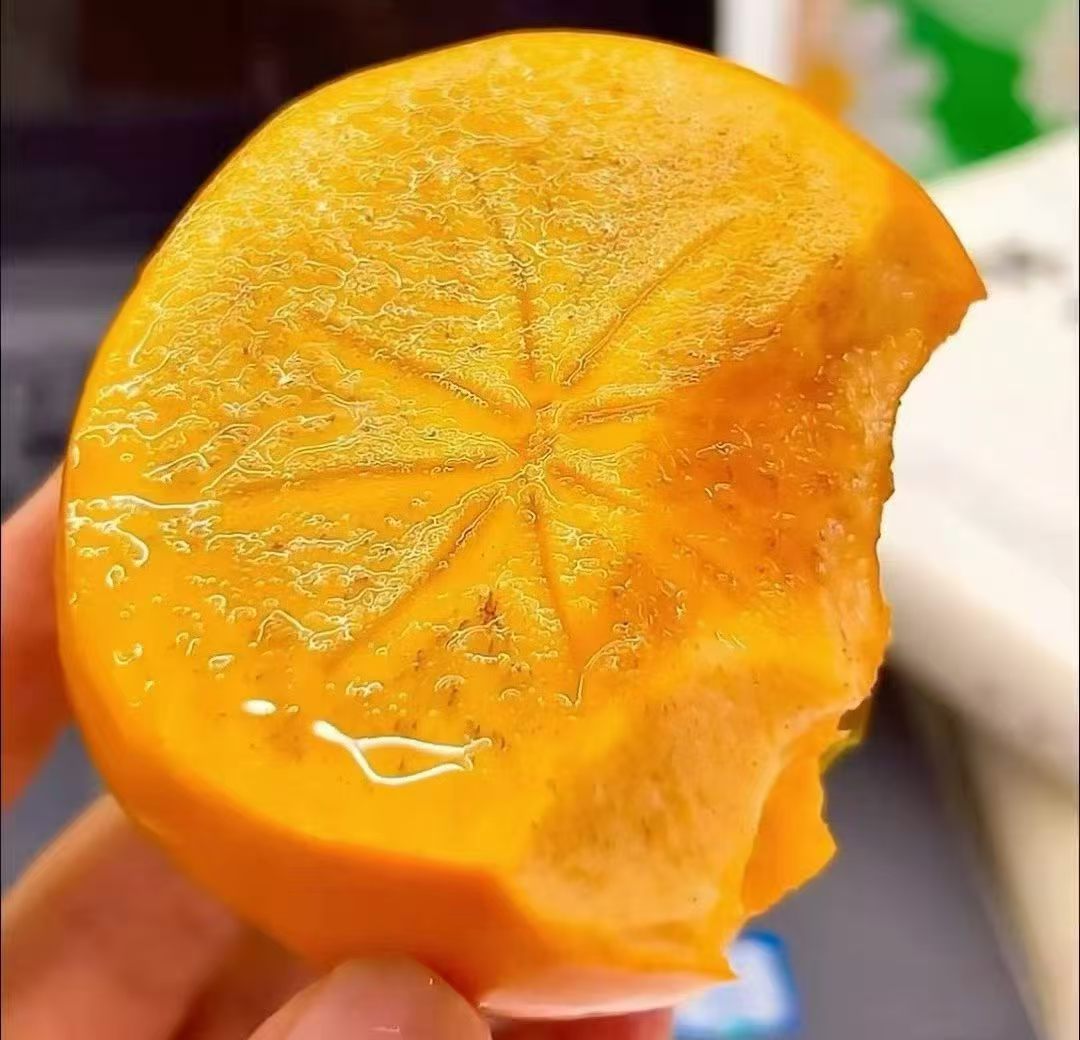 Primo piano della polpa: rosso-arancio traslucido, croccante e succosa, con un nucleo chiaro a forma di stella - la firma di un cachi PCNA.